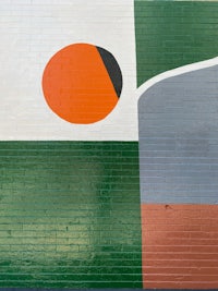 a painting of a green, orange, and black circle on a brick wall